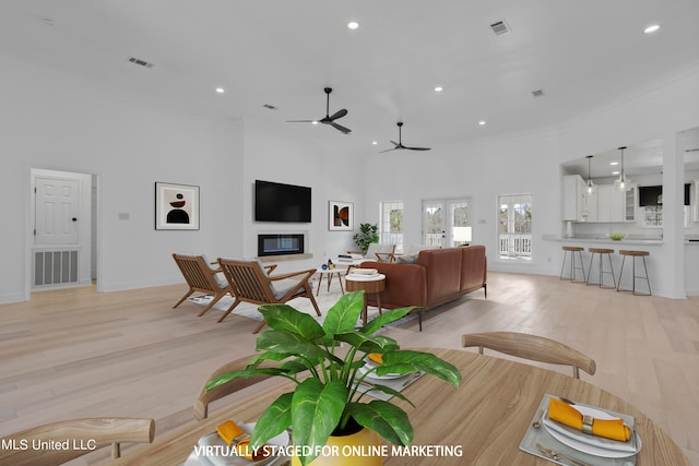 living room featuring ceiling fan, crown molding, a towering ceiling, and light wood-type flooring