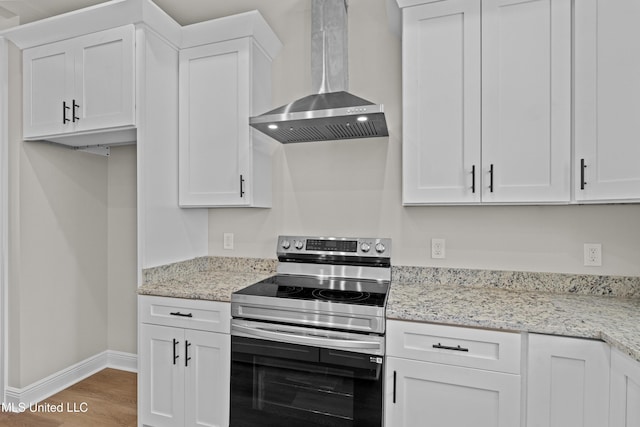 kitchen with light stone counters, stainless steel electric stove, wall chimney range hood, white cabinets, and hardwood / wood-style floors