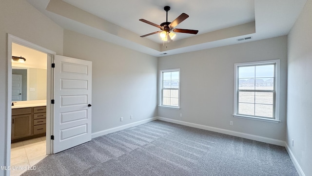 unfurnished bedroom featuring connected bathroom, a tray ceiling, light colored carpet, and ceiling fan