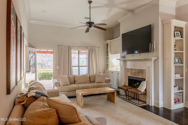 living room featuring built in shelves, ornamental molding, wood-type flooring, and ceiling fan