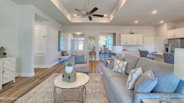 living room featuring hardwood / wood-style flooring, ceiling fan, a raised ceiling, and ornamental molding