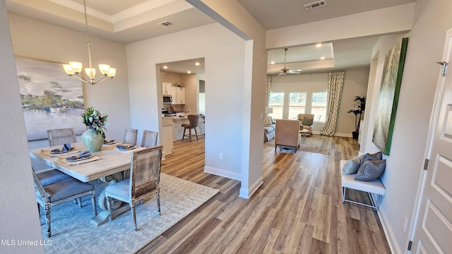 dining space with hardwood / wood-style floors, ceiling fan with notable chandelier, and a tray ceiling