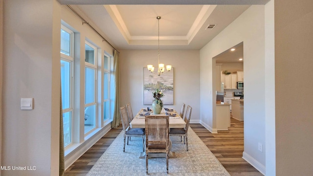 dining area with a chandelier, a tray ceiling, and dark wood-type flooring