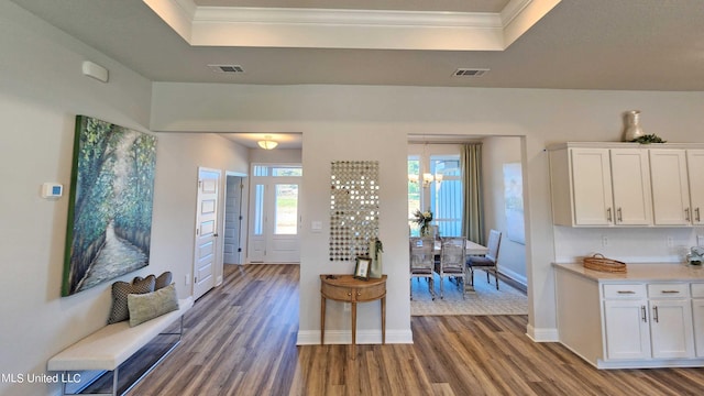 interior space featuring a raised ceiling, ornamental molding, a notable chandelier, and hardwood / wood-style flooring