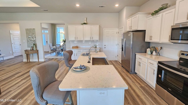 kitchen featuring appliances with stainless steel finishes, sink, wood-type flooring, white cabinetry, and an island with sink