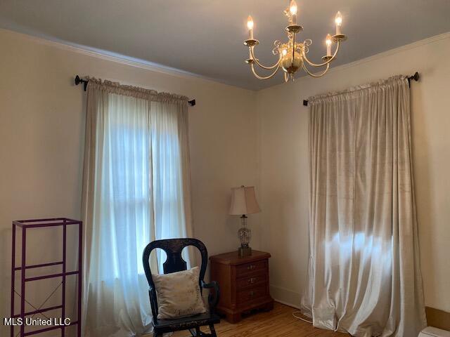 sitting room with hardwood / wood-style flooring, crown molding, and an inviting chandelier