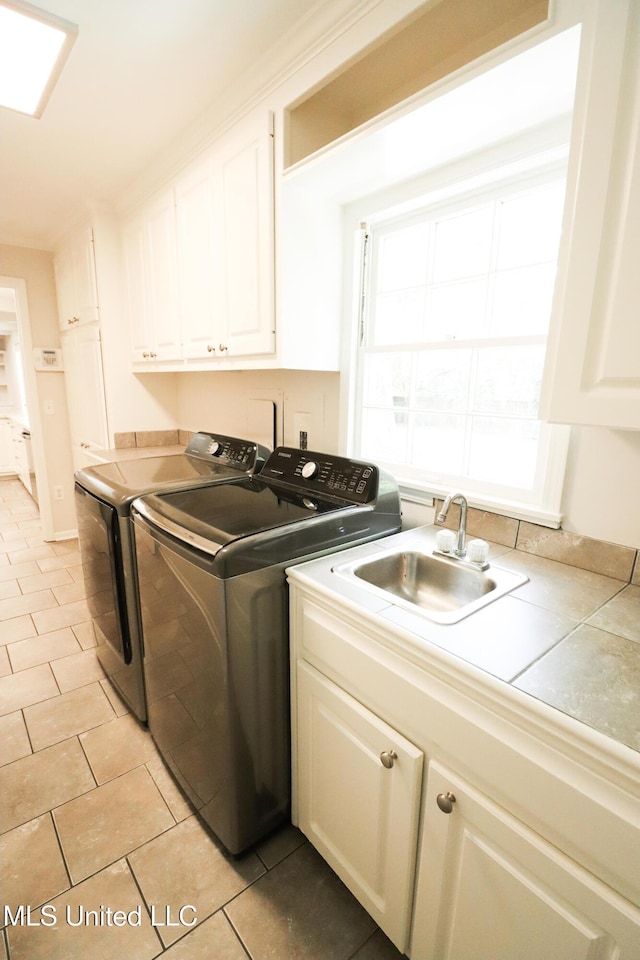 laundry area with cabinet space, light tile patterned floors, separate washer and dryer, and a sink