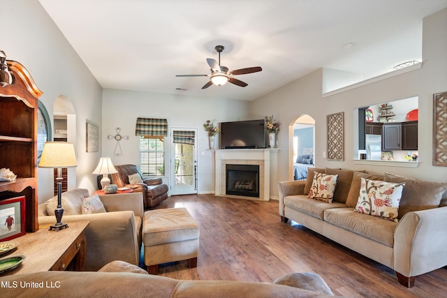 living room featuring arched walkways, a fireplace, wood finished floors, a ceiling fan, and vaulted ceiling