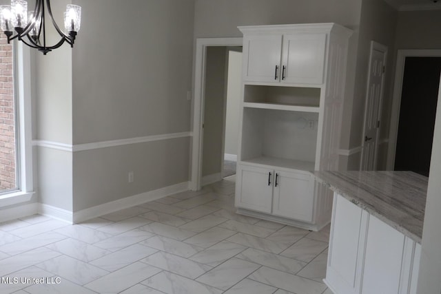unfurnished dining area with a chandelier, light marble finish flooring, and baseboards