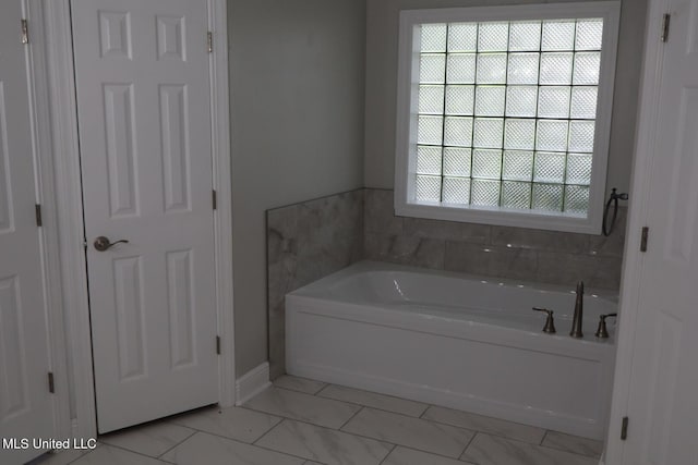 bathroom with a garden tub, baseboards, and marble finish floors