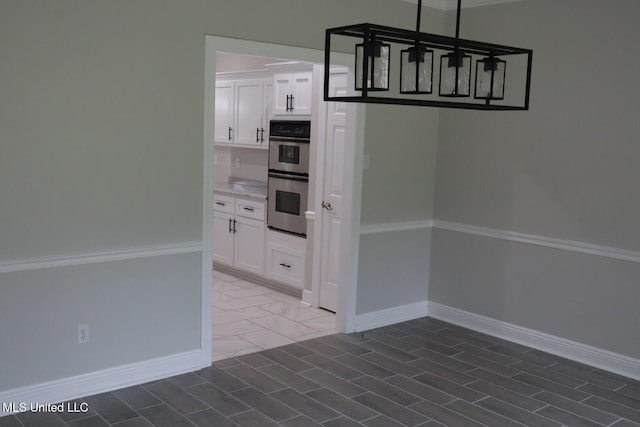 kitchen featuring double oven, white cabinets, baseboards, light countertops, and dark tile patterned floors