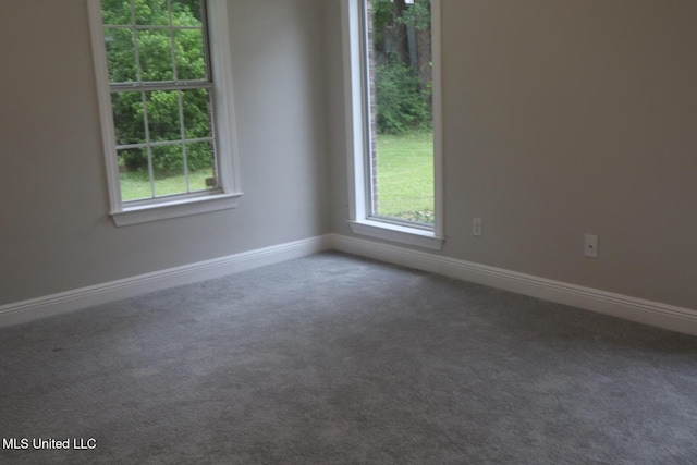 unfurnished room featuring dark carpet, healthy amount of natural light, and baseboards