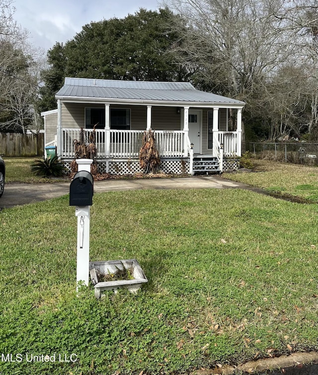 view of front facade with a front yard, covered porch, fence, and metal roof