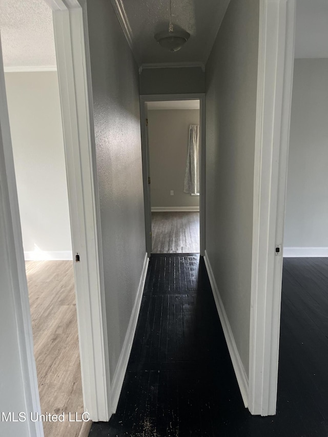 corridor featuring crown molding, a textured ceiling, baseboards, and wood finished floors