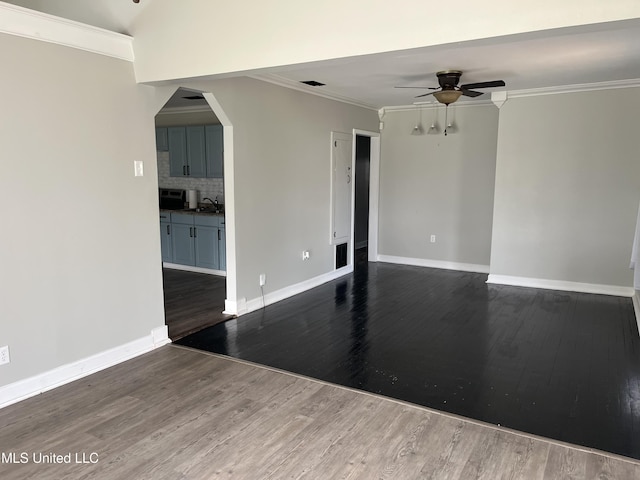 spare room with dark wood-type flooring, arched walkways, crown molding, and a ceiling fan