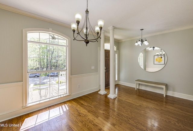 unfurnished dining area with a notable chandelier, crown molding, ornate columns, and dark hardwood / wood-style flooring