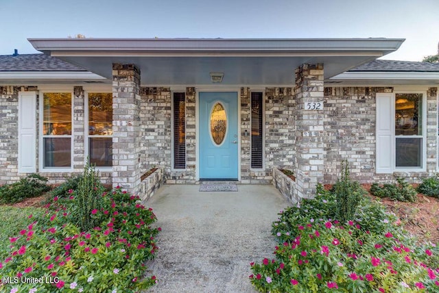 entrance to property featuring a shingled roof, covered porch, and brick siding