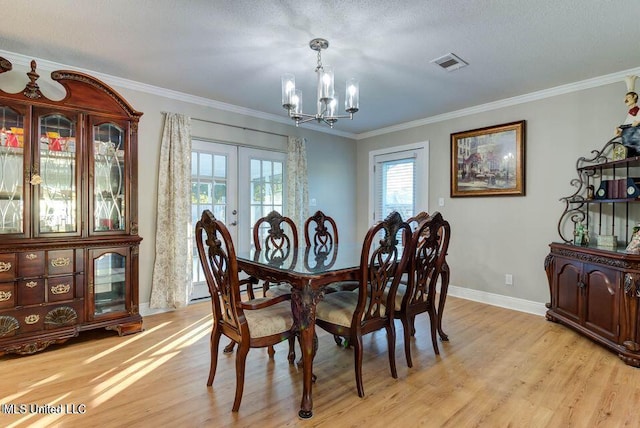 dining space with visible vents, light wood-style flooring, ornamental molding, an inviting chandelier, and french doors