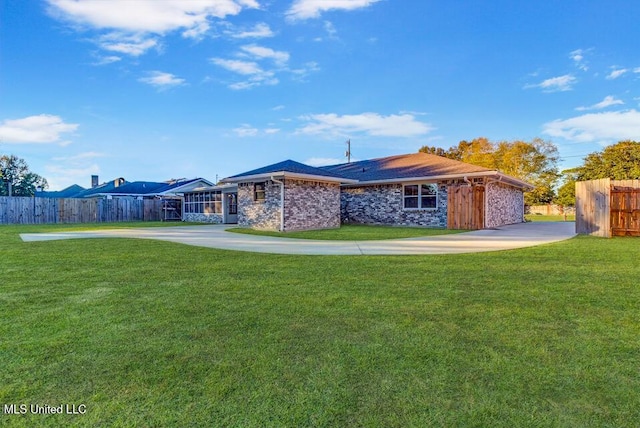 back of house with driveway, fence, a lawn, and brick siding