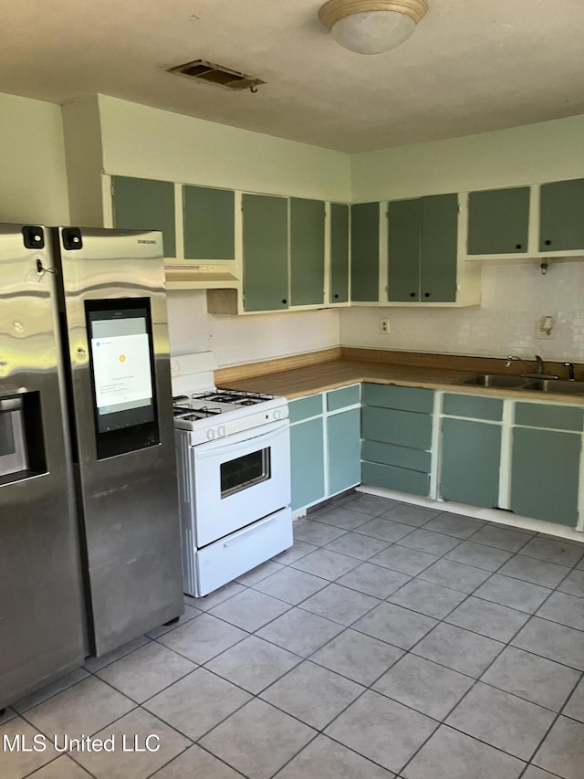 kitchen featuring white range with gas stovetop, green cabinets, a sink, light tile patterned floors, and under cabinet range hood