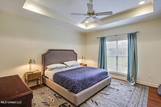 bedroom with a raised ceiling, ornamental molding, wood finished floors, baseboards, and recessed lighting
