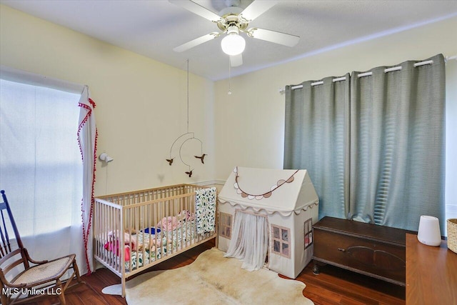 bedroom with wood finished floors, a crib, and a ceiling fan
