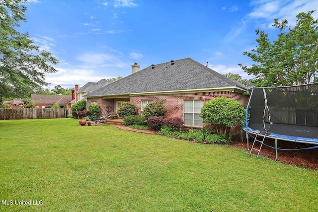 rear view of house with a trampoline, brick siding, and a shingled roof