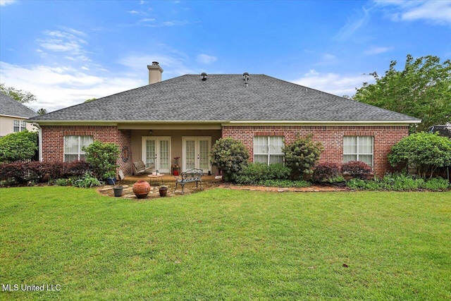 rear view of property featuring french doors, a chimney, a lawn, and brick siding