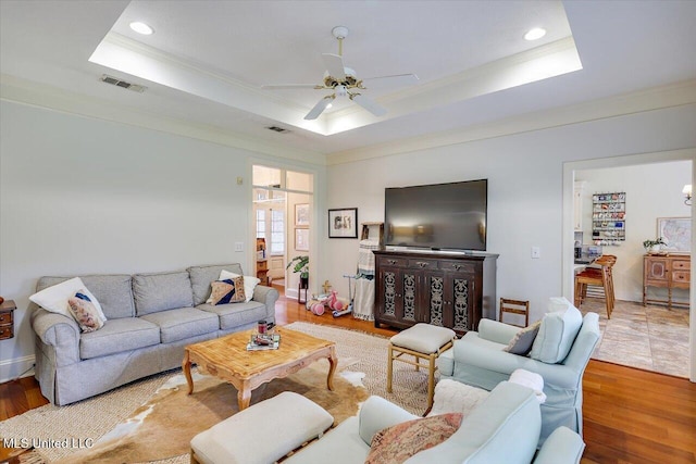 living area with ornamental molding, a tray ceiling, wood finished floors, recessed lighting, and ceiling fan