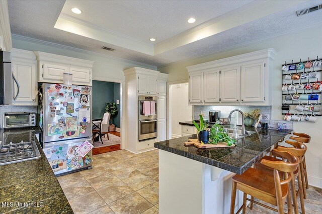 kitchen featuring stainless steel appliances, a peninsula, backsplash, white cabinetry, and ornamental molding