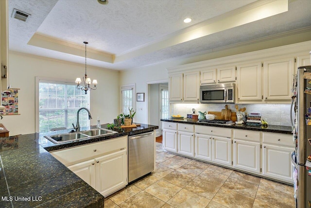 kitchen featuring stainless steel appliances, a tray ceiling, a sink, ornamental molding, and backsplash