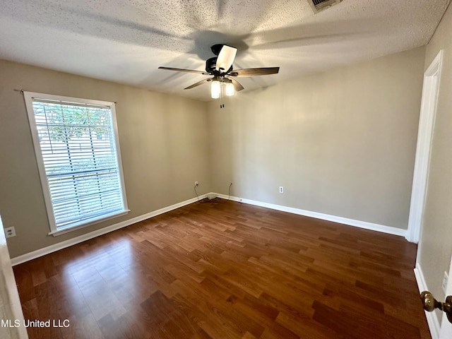 spare room with a textured ceiling, dark wood-type flooring, a ceiling fan, and baseboards