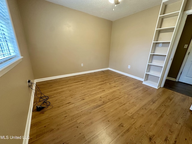 interior space with a textured ceiling, baseboards, and wood finished floors