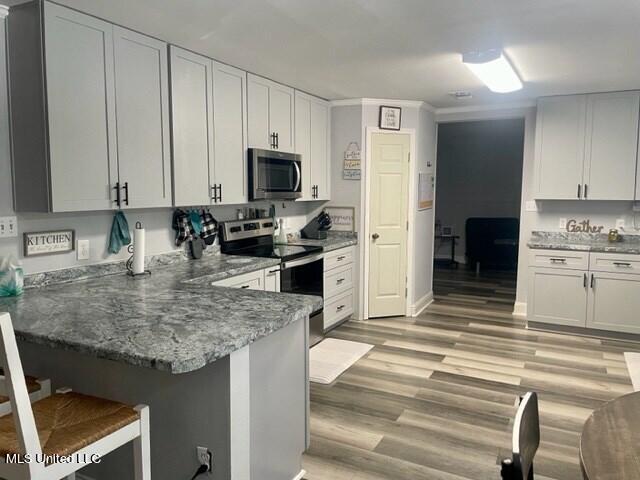 kitchen featuring light hardwood / wood-style flooring, kitchen peninsula, a breakfast bar, white cabinetry, and appliances with stainless steel finishes