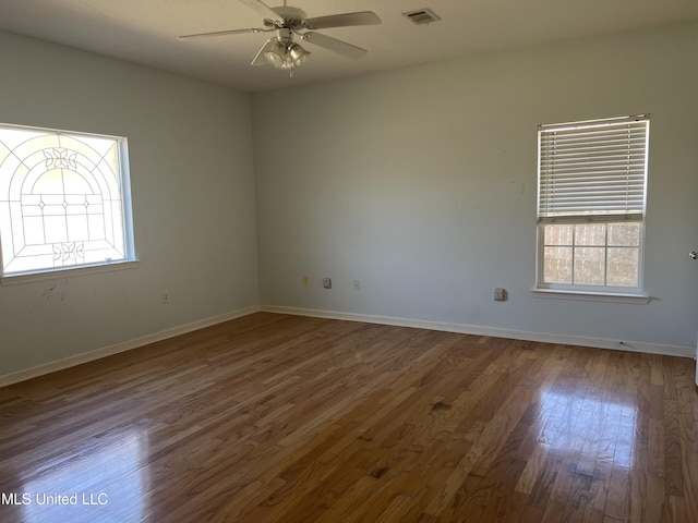 spare room with a ceiling fan, visible vents, wood finished floors, and baseboards