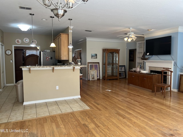 kitchen featuring a breakfast bar area, light stone counters, visible vents, light wood-style flooring, and freestanding refrigerator