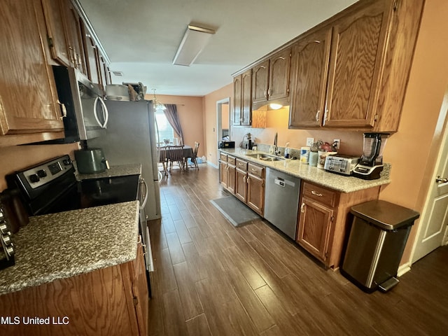 kitchen featuring light stone counters, a sink, dark wood-type flooring, appliances with stainless steel finishes, and brown cabinets