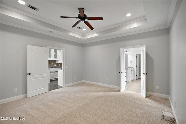 unfurnished bedroom with ceiling fan, light colored carpet, ensuite bath, and a raised ceiling