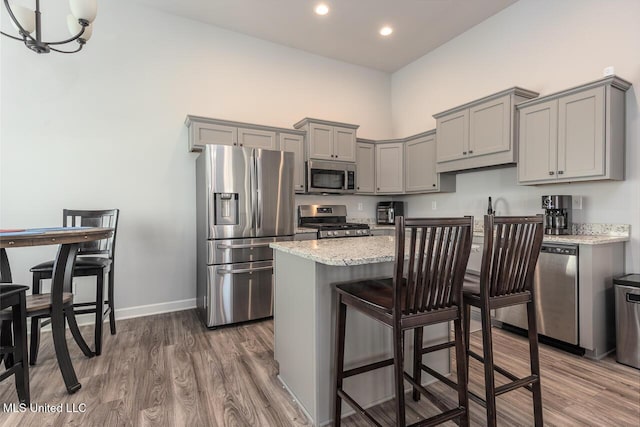 kitchen with appliances with stainless steel finishes, gray cabinetry, a center island, wood-type flooring, and light stone countertops