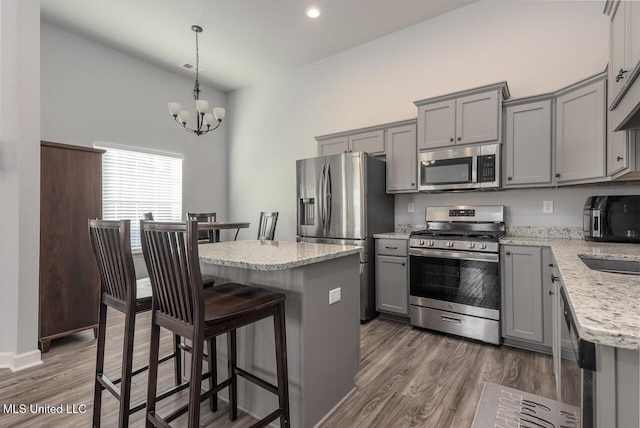 kitchen featuring dark wood-type flooring, light stone counters, decorative light fixtures, a kitchen island, and stainless steel appliances