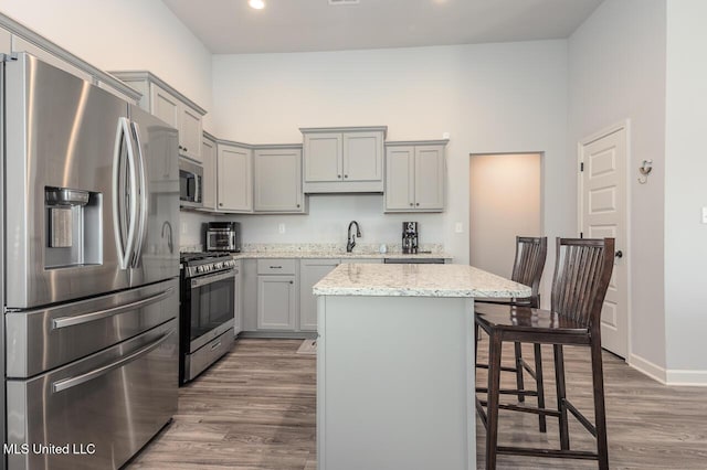 kitchen featuring a breakfast bar area, hardwood / wood-style flooring, a center island, stainless steel appliances, and light stone countertops