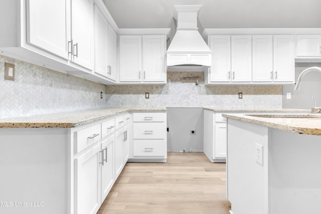 258 Memphis Ave, Holly Springs, MS 38635 - kitchen with custom range hood, light stone countertops, light wood-style flooring, decorative backsplash, and white cabinetry