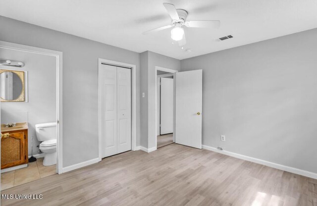unfurnished bedroom featuring ensuite bathroom, a closet, light wood finished floors, and baseboards