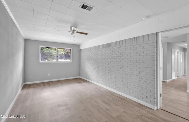 unfurnished room with wood finished floors, brick wall, baseboards, visible vents, and a ceiling fan