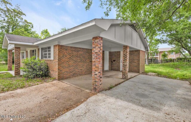 view of property exterior with driveway, board and batten siding, an attached carport, and brick siding