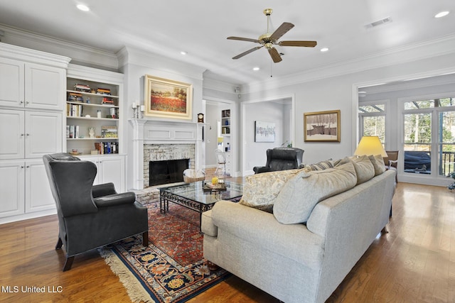 living room featuring ornamental molding, ceiling fan, built in features, a fireplace, and hardwood / wood-style floors