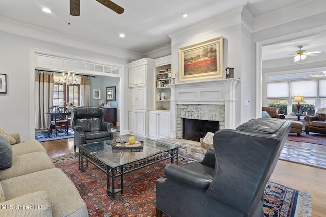 living room with a fireplace, hardwood / wood-style floors, ceiling fan with notable chandelier, and ornamental molding