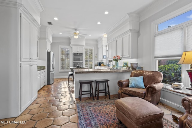 kitchen featuring kitchen peninsula, stainless steel fridge, a kitchen bar, ceiling fan, and white cabinetry