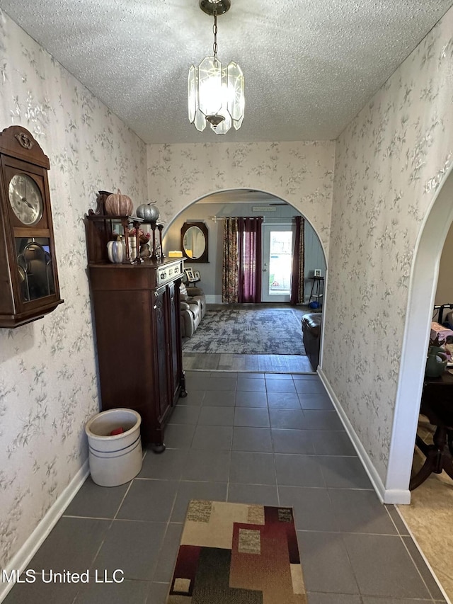 hallway with a textured ceiling, an inviting chandelier, and dark tile patterned floors