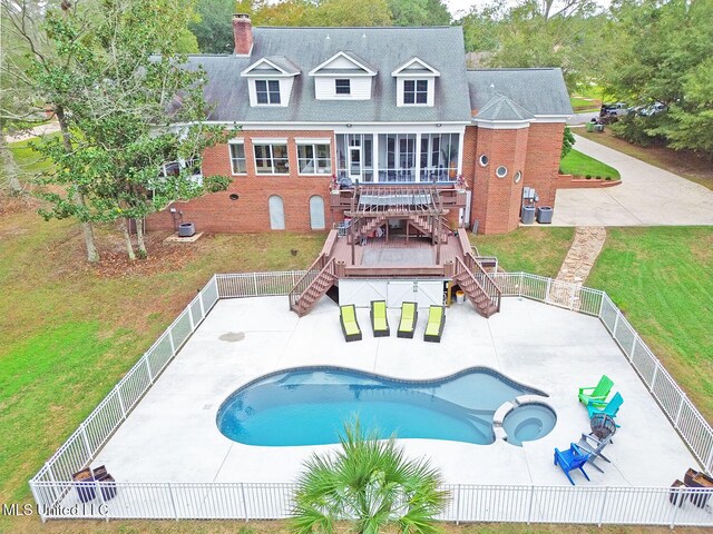 rear view of property featuring a yard, a pool with hot tub, a patio area, and a sunroom